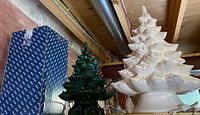 Photo showing both ceramic Christmas trees on a shelf with insulation and plumbing pipes in background.