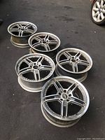 Five aluminum tire rims arranged on the ground, showing the top face of the rims and their design features, including the five spokes and bolt holes.