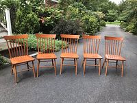 Set of five cherry wood Shaker-style kitchen chairs arranged outdoors on pavement, showing shape, style, and condition including visible wear and repairs.