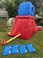 Full view of inflated red, blue, and yellow slide along with orange air blower, yellow hose, and four blue anchor sandbags laid out in front