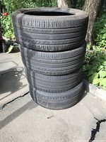 Stack of 4 Michelin tires outdoors on pavement next to greenery