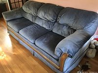 Sofa upholstered in blue-gray corduroy fabric with wooden trim accents, positioned on hardwood floor near windows.