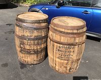 Two oak whiskey barrels outdoors revealing original branding and iron bands in weathered condition.
