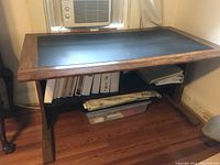 Side angle showing wooden legs and storage shelf below the desk surface with binders and plastic bin.