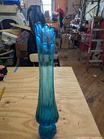 Full height view of the 20-inch blue glass vase on a wooden table showing the scalloped ruffled top and ribbed body.