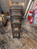 View of four nested wooden stands with glass tops and carved fruitwood panels under glass.