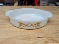 Round white glass casserole or cake pan with wheat design on the side, showing exterior view and handles.