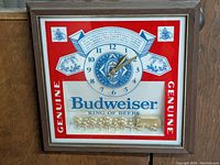 Full front view of the square Budweiser branded wall clock with horse team figurine and wood-tone frame.