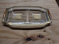 Top angled view of the clear glass divided serving tray with gold circular designs and teak wood handles on a wooden surface.