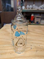 Photo of clear glass jar with fitted lid showing blue and gold boomerang and amoeba shapes scattered around the jar body.