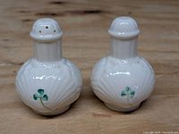 Front-facing view of pair of white porcelain sea shell salt and pepper shakers with green shamrock decoration showing detail of texture and colors.