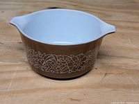 Photo of Pyrex casserole dish showing brown exterior with white floral Woodland pattern, round shape with two spout handles, white interior.