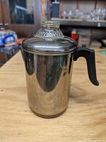 Front angle view showing the metal body, black handle, and glass lid knob of the six-cup coffee percolator.