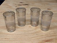 Four clear glass tumblers placed upright on a wooden surface showing platinum ring decorations and frosted band in excellent condition.