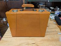 Front view of the small tan leatherette locking travel case with handle on top.