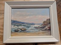 Framed oil painting on board showing a seascape with waves, rocks, and a distant sailboat, under a partly cloudy sky.