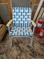 Front view of vintage aluminum framed folding lawn rocking chair with blue and white webbed seat and backrest and wooden armrests on a wooden floor.
