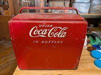 Front view of a red metal Coca Cola ice chest cooler with 'Drink Coca-Cola in Bottles' white lettering.