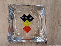 Photo of front face of square glass ashtray showing colorful Tourinns logo in black, yellow, and red stacked diamonds reading 'Tourinns Modern Motor Court Motel'.