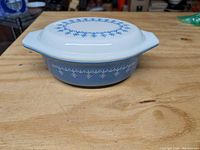 Front angled view of vintage Pyrex covered casserole dish showing blue snowflake design on lid and blue border on dish