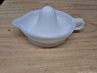 White/milk glass juice reamer placed on wooden surface, angled to show side with handle and spout