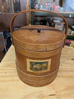 Front view of wooden firkin with lid and handle, showing vintage image on front and black knob on lid.