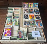 Box of stacked baseball cards with binder pages and loose cards visible, plus sealed pack of Score baseball cards.