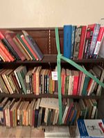 Books of various colors and sizes on a dark wooden bookshelf, arranged in three rows, secured with a green strap