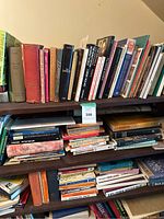 Full view of three shelves filled with a large number of mixed books in various conditions and sizes, stacked vertically and horizontally to fit space.