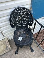 Full view of the black cast iron chair with detailed floral backrest and circular seat design, showing outdoor placement.