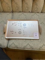 Rectangular metal serving tray with etched cornflower floral pattern and two extended handles placed on patterned fabric couch.