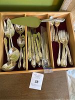 Wooden flatware chest with compartments showing knives, forks, spoons and serving pieces laid out