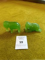 Photo showing two green jade elephant figurines on a yellow carpet, one standing and one resting, alongside auction lot number card.
