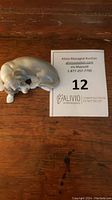 Photo of the Lladro porcelain dog figurine on a wooden surface with auction label visible.