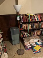 Full view of the floor lamp showing base, pole, and milk glass shade unlit near a bookshelf and filing cabinet.