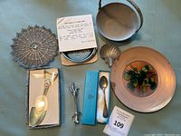 Image showing variety of copper, brass, and silver metal items arranged on a table including bowls, plates, spoons, and decorative items.