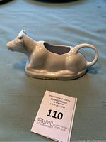 Side view of the white glazed reclining cow creamer showing overall shape and glaze condition