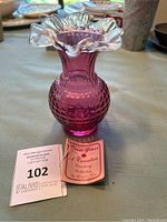 Photo showing the purple vase with hobnail pattern and clear ruffled top with the Rossi Glass Canadian Country Collection tag and auction tag beside it.