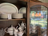 Cabinet shelf showing stacked dinner plates, salad plates, cups, saucers and tea/coffee service pieces