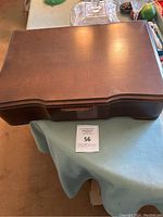 Closed wooden silverware storage box with handle on front and some surface wear marks.