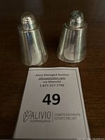 Two sterling silver salt and pepper shakers side by side with auction lot tag in front