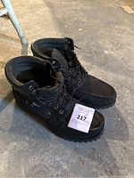 Pair of black Timberland moc toe boots, showing front-right angled view, laces tied and boots standing on concrete floor.