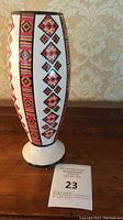 Tall oval ceramic vase showing detailed Ukrainian geometric and floral patterns in red, black, yellow, and white on a white background, standing on wooden surface.