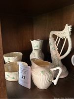Shelf display of six small Belleek porcelain shamrock-decorated items, including harp figurine and small vases
