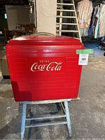 Front view of red metal Coca Cola cooler showing Coca Cola logo and handle on top