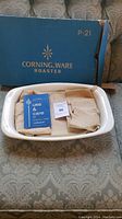 Vintage Corningware white ceramic roaster in original blue box with use & care booklet and packaging paper inside.