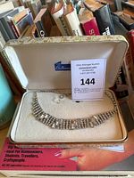 Wide view of vintage rhinestone necklace in a cream-colored Astana box showing the necklace detail and vintage box with books in background.