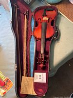 Violin inside an open hard case with visible horsehair bow and a repair card inside the case.