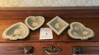 Four Wedgwood Jasperware playing card dishes laid out on a wooden surface showing their shapes and white relief details.