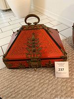 Front view of triangular red lacquer chest with brass detailing, handle and clasp